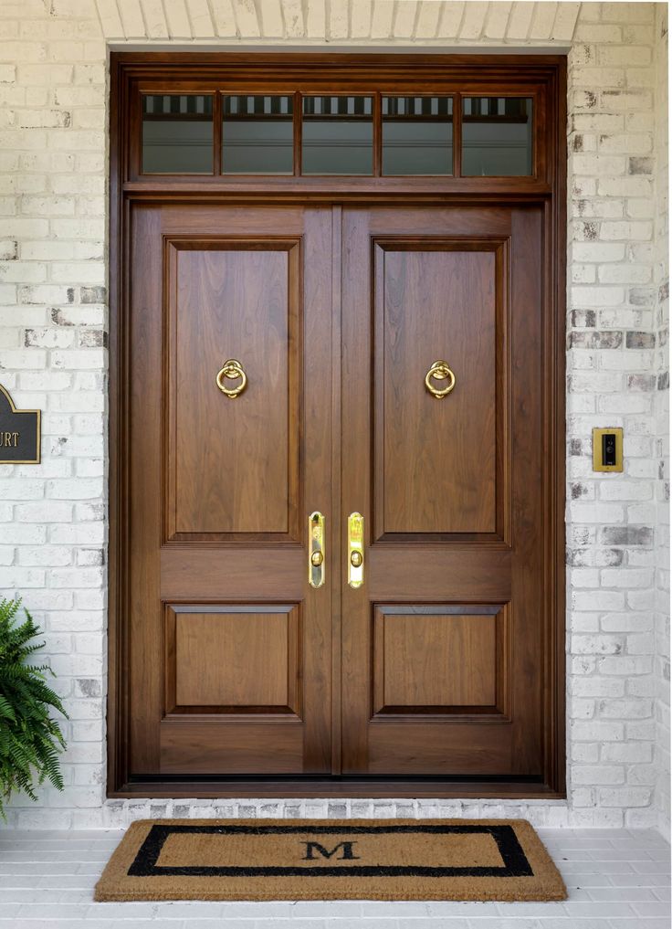 the front door to a home with two wooden doors and a welcome mat on the floor