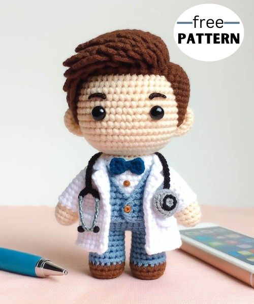 a crocheted doctor doll next to a cell phone and pen on a table