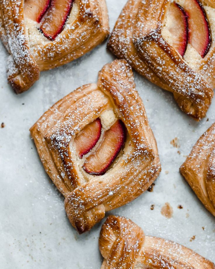 several pastries covered in powdered sugar on top of a white countertop with strawberries