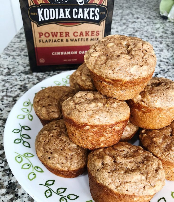 a pile of muffins sitting on top of a white plate next to a box of kodiak cakes