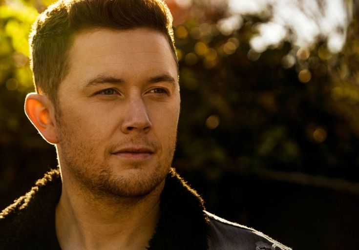 a close up of a person wearing a jacket and looking off to the side with trees in the background