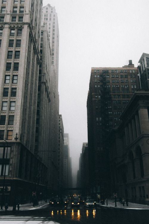 an empty city street with tall buildings in the background on a foggy, overcast day