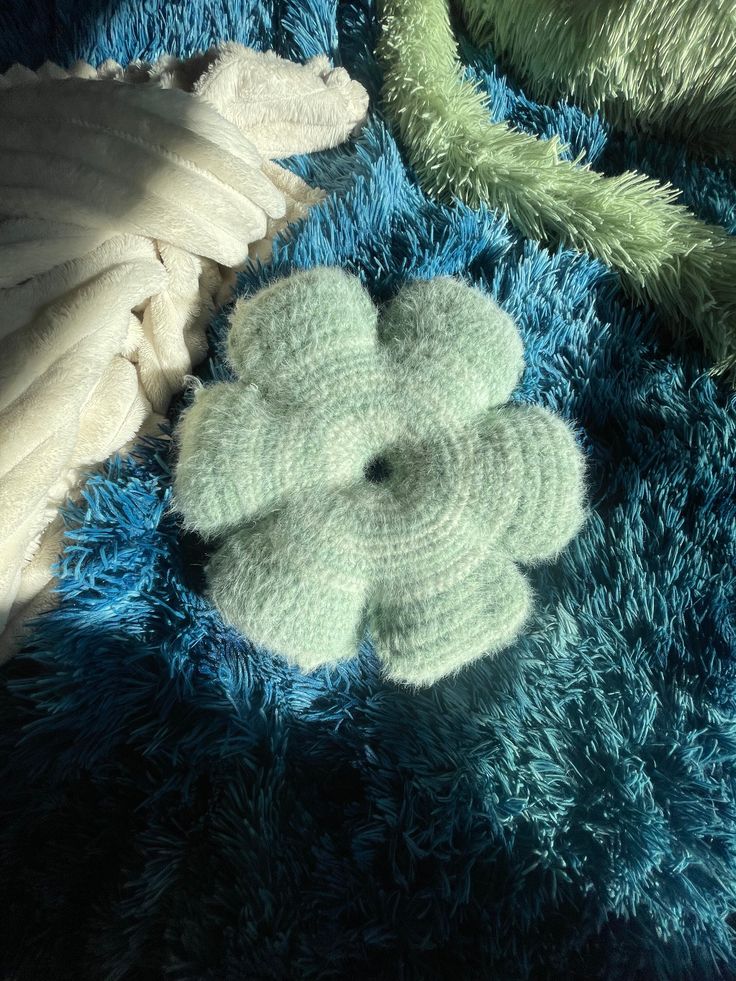 there is a crocheted flower on the blue carpet next to some white feathers