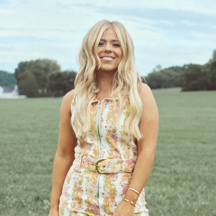 a woman standing in the grass with her hand on her hip and smiling at the camera