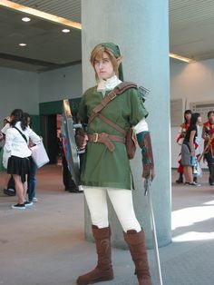 a woman dressed as link from the legend of zelda cosplaying in front of a column