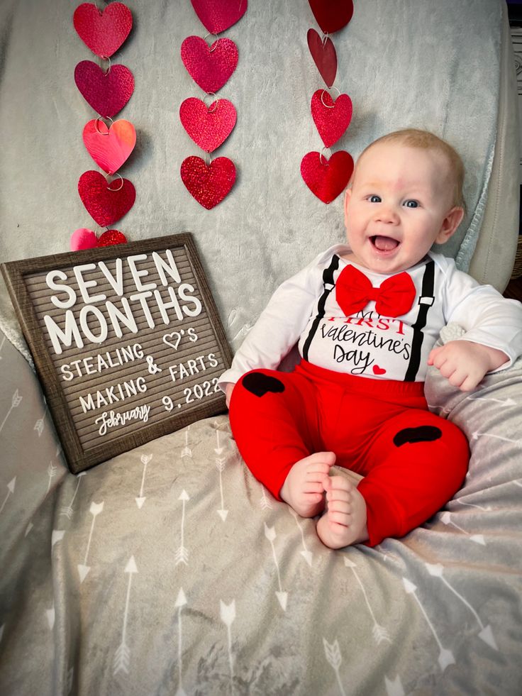 a baby sitting on top of a bed with hearts hanging from the wall behind him