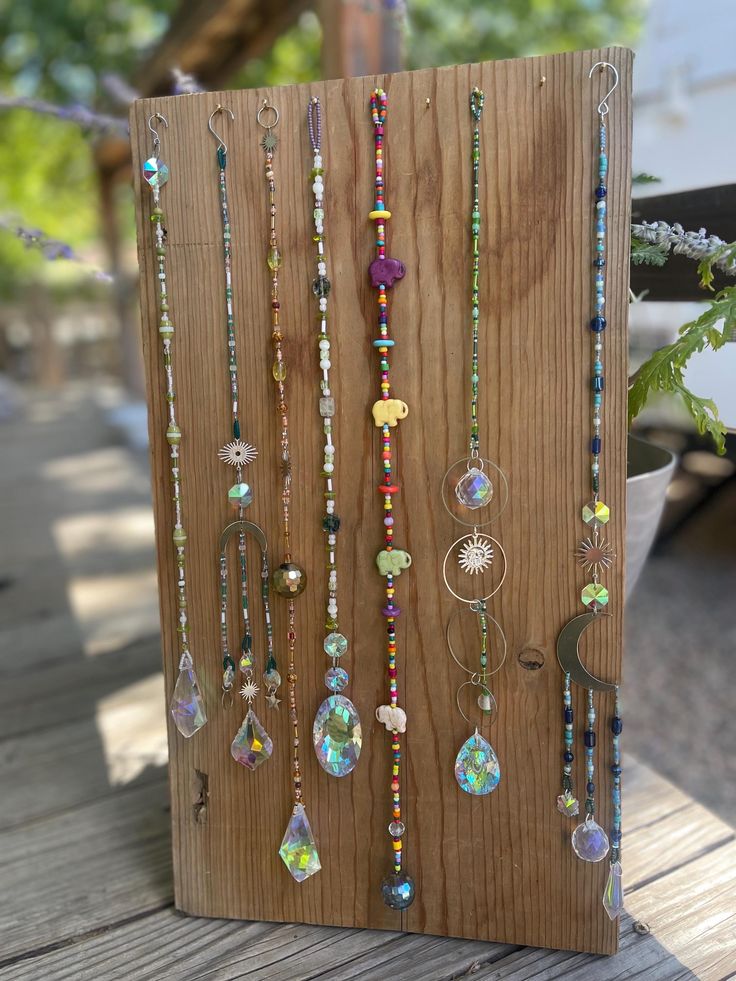 a wooden board with many different necklaces hanging on it's sides and a potted plant in the background