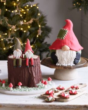 two gnomes sitting on top of a table next to a christmas tree and cookies