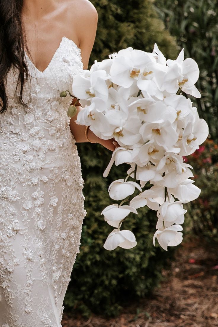 a woman in a wedding dress holding a bouquet of white orchids with her hand