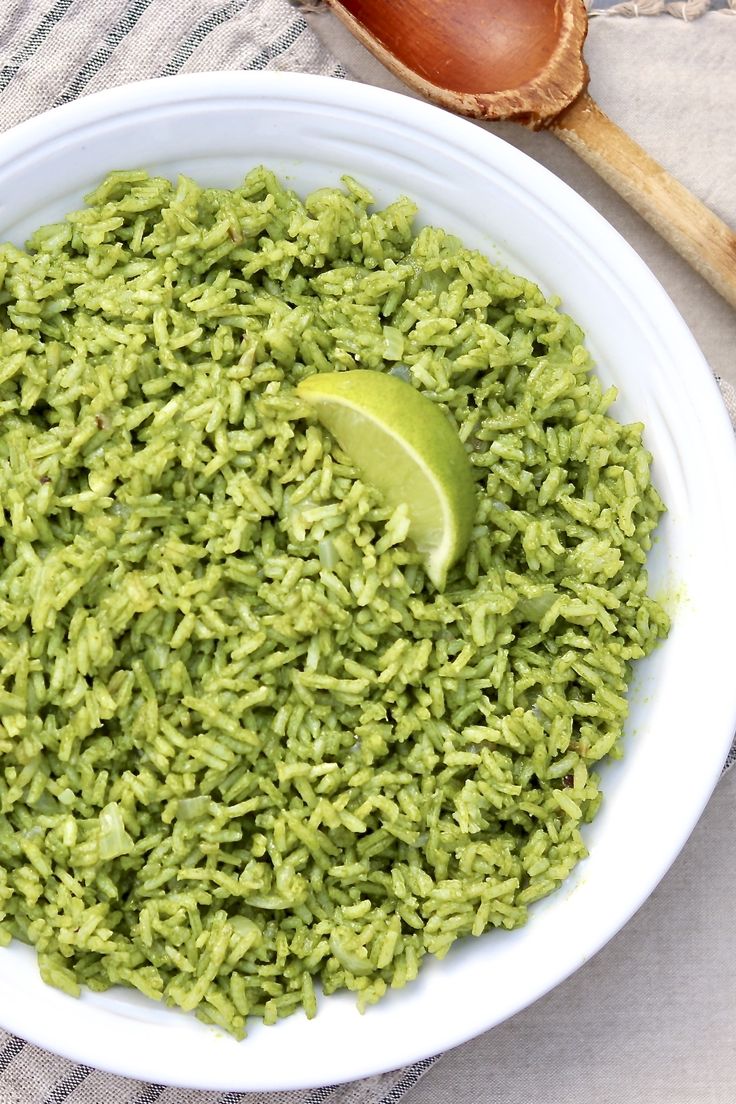 a white bowl filled with green rice and a wooden spoon on top of a table