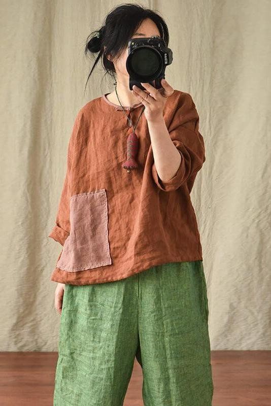 a woman holding a camera up to her face while wearing green pants and a brown shirt