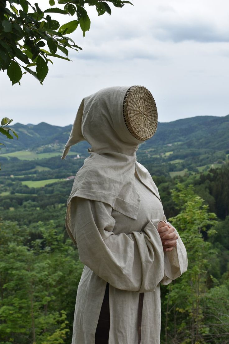 a woman in a white robe and bonnet looking out over the valley from a hill