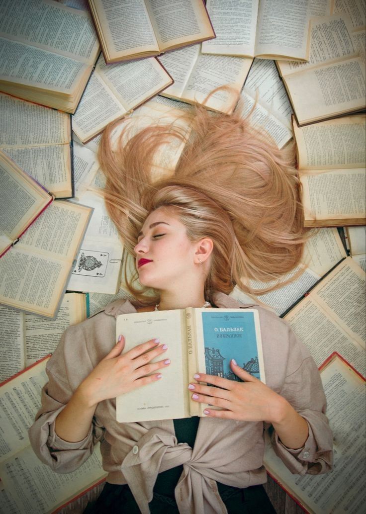 a woman laying on top of books with her hair blowing in the wind while holding an open book