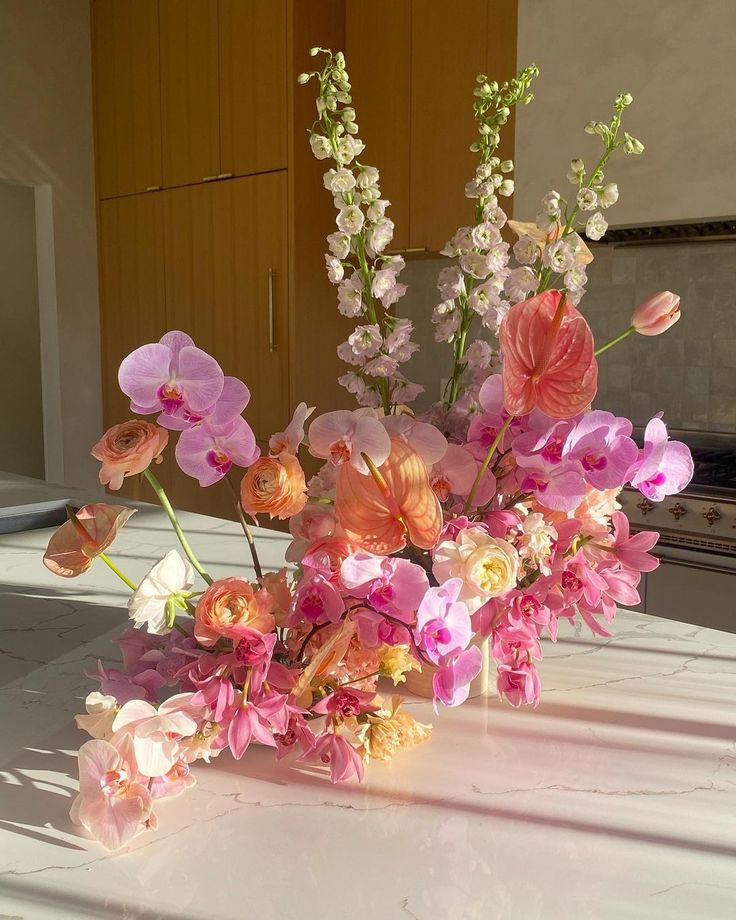 a vase filled with pink and white flowers on top of a table in a kitchen