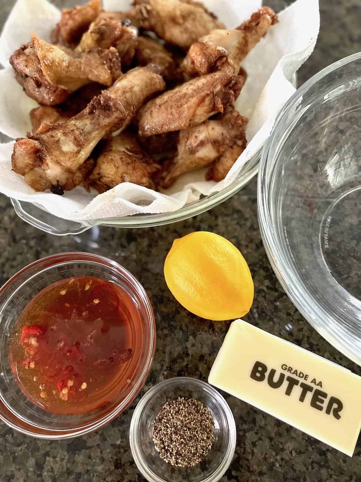 some chicken wings and seasoning in bowls on a granite counter top with a sign that says butter