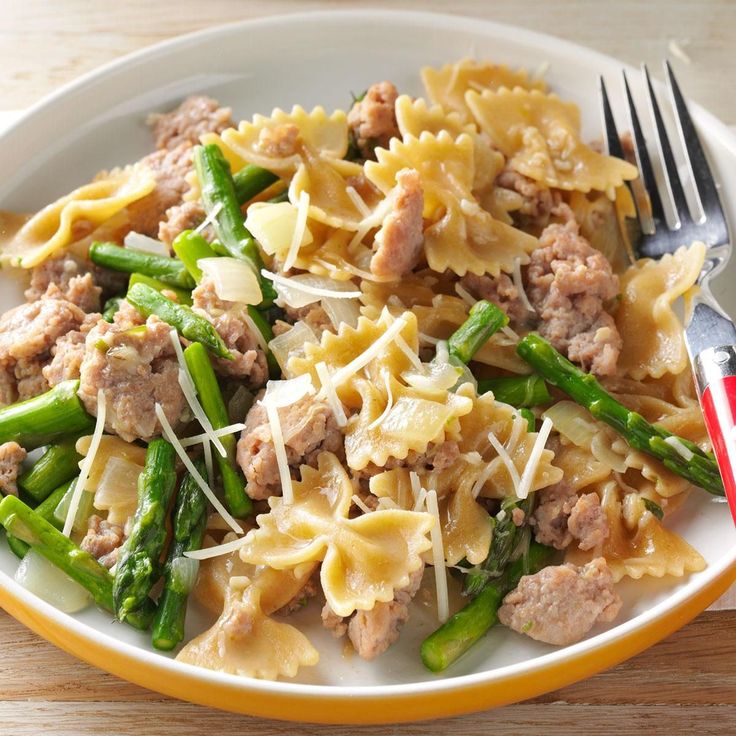 a white plate topped with pasta and asparagus next to a knife and fork