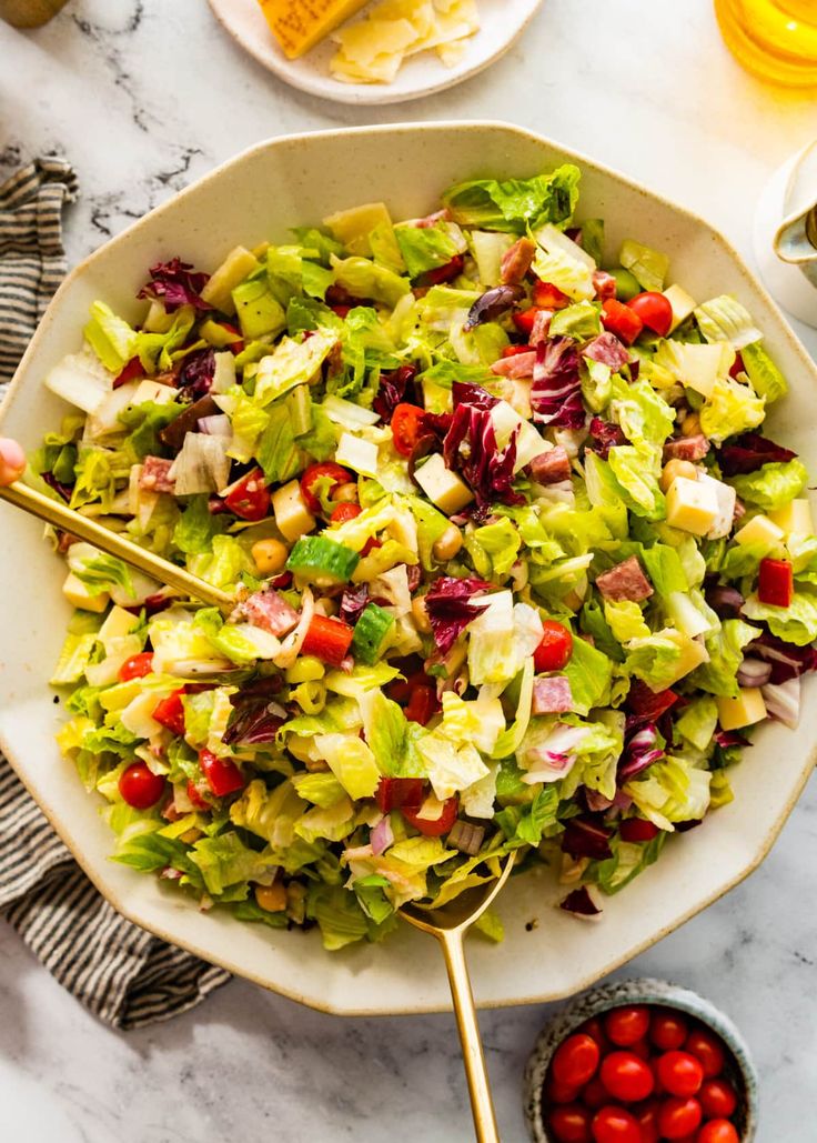 a salad with lettuce, tomatoes and dressing in a white bowl on a marble table