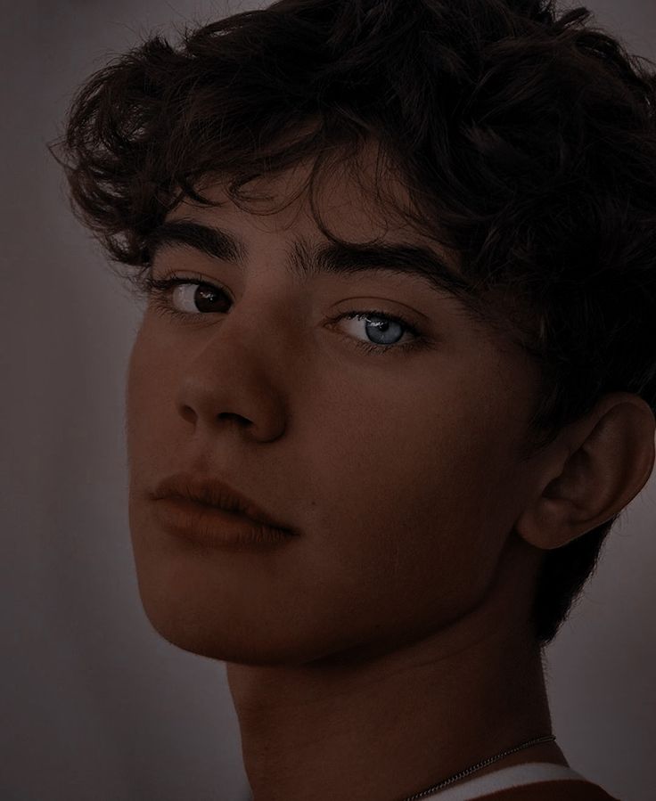 a close up of a person with blue eyes and curly hair, wearing a brown shirt