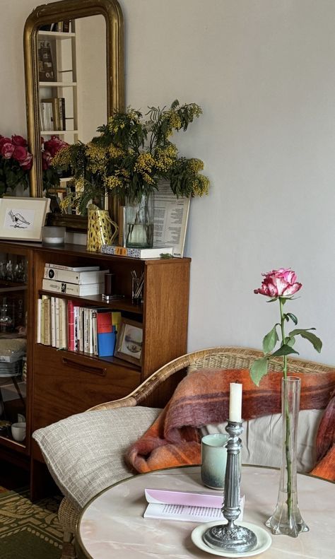 a living room filled with furniture and flowers on top of a white table next to a book shelf