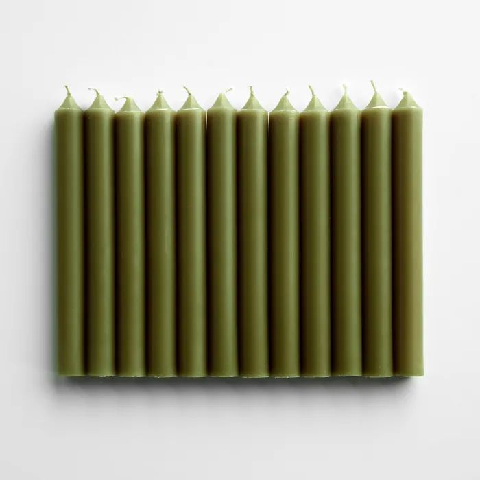 six green candles lined up against a white wall