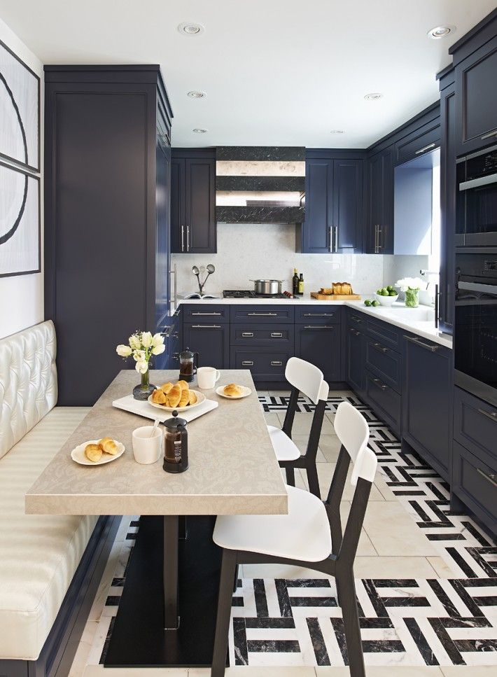 a kitchen with black cabinets and white dining room chairs in front of a table that has two plates of food on it