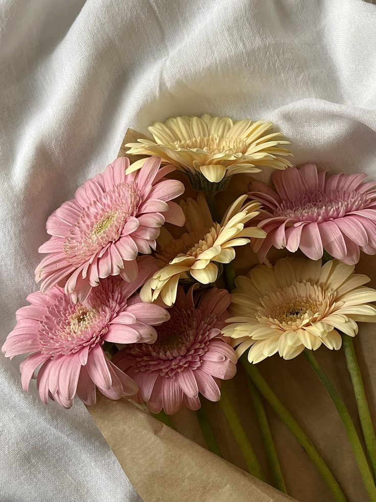 a bunch of pink and yellow flowers sitting on top of a white sheet