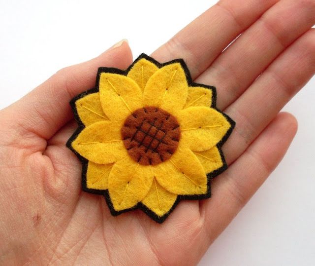 a hand holding a yellow and brown flower brooch