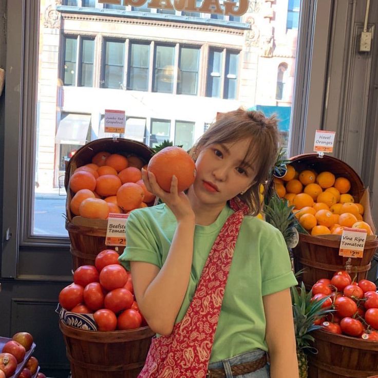 a woman is holding an orange in front of some fruit at a store window display