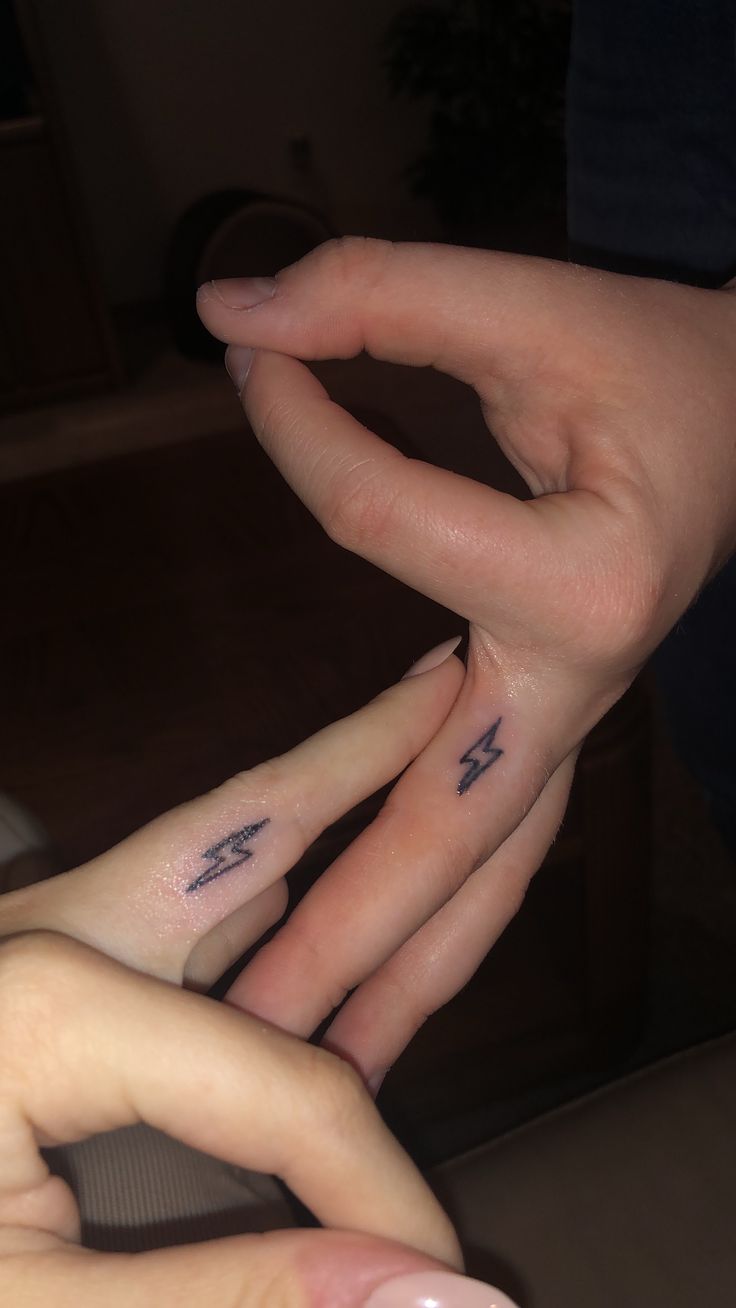 two people holding hands with tattoos on their fingers