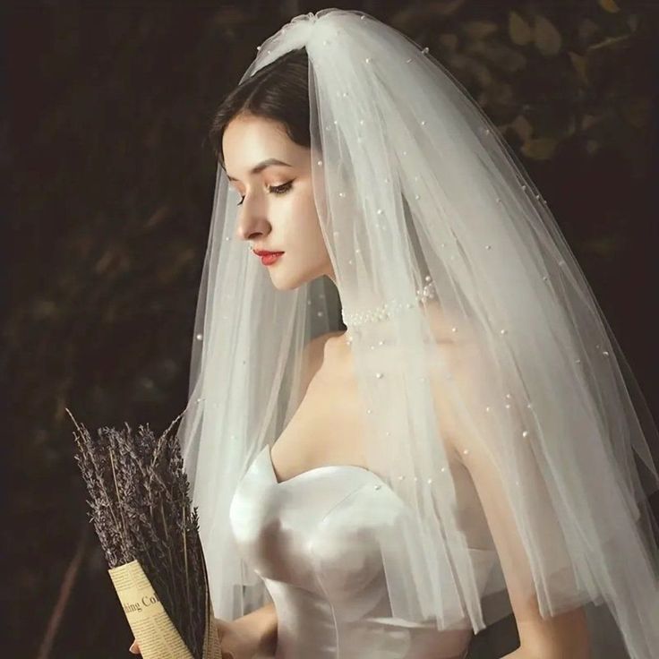 a woman wearing a wedding dress and veil holding a flower in her hand while posing for the camera