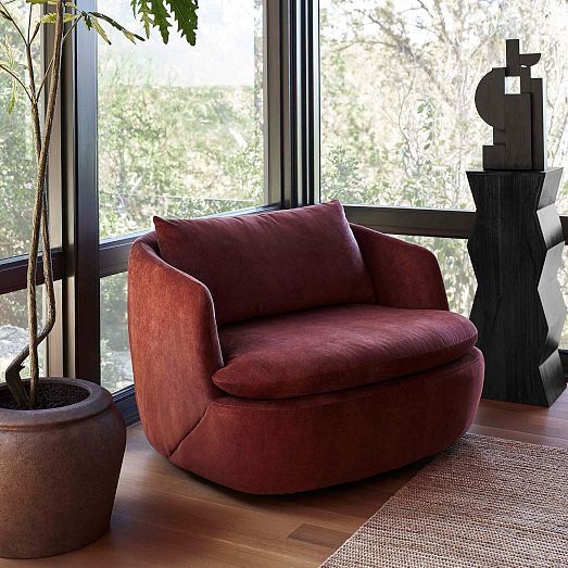 a red chair sitting in front of a window next to a potted plant on top of a wooden floor