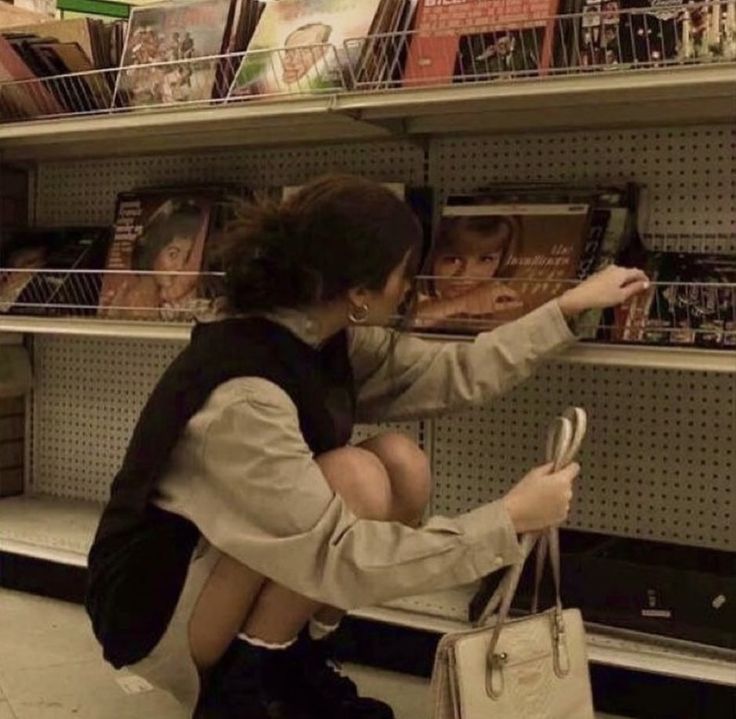 a woman sitting on the ground in front of a book shelf holding onto a purse