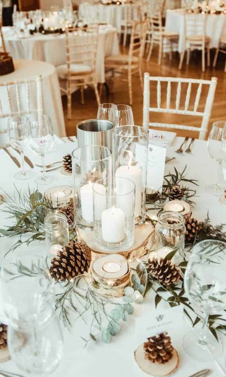 a table topped with lots of white tables covered in candles and pineconis on top of it