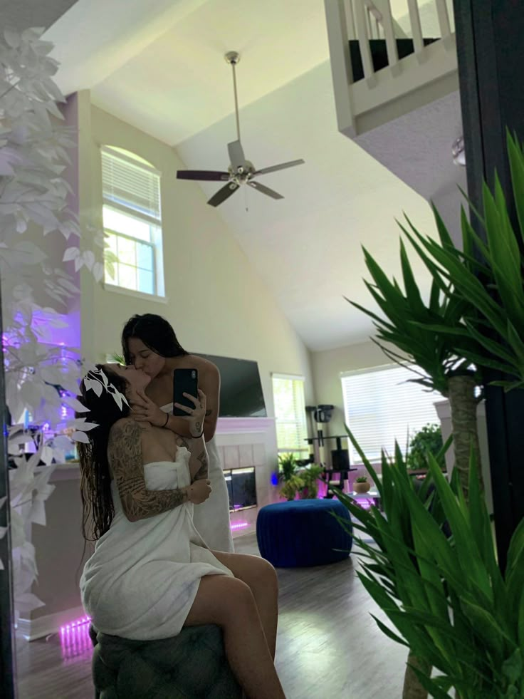 a woman sitting on top of a chair next to a plant in a room with white walls