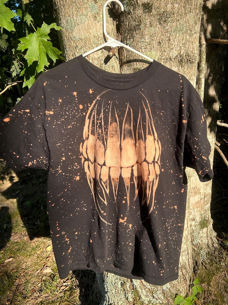 a t - shirt hanging on a tree in front of a tree with leaves and dirt all over it