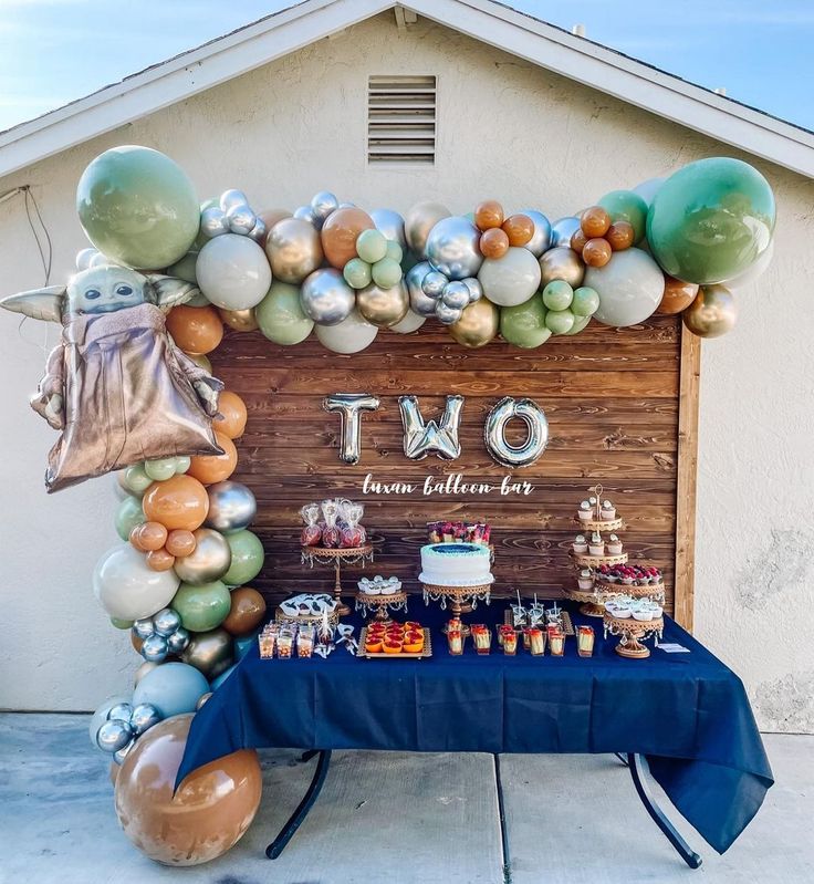 a table topped with balloons and desserts next to a sign that says two on it