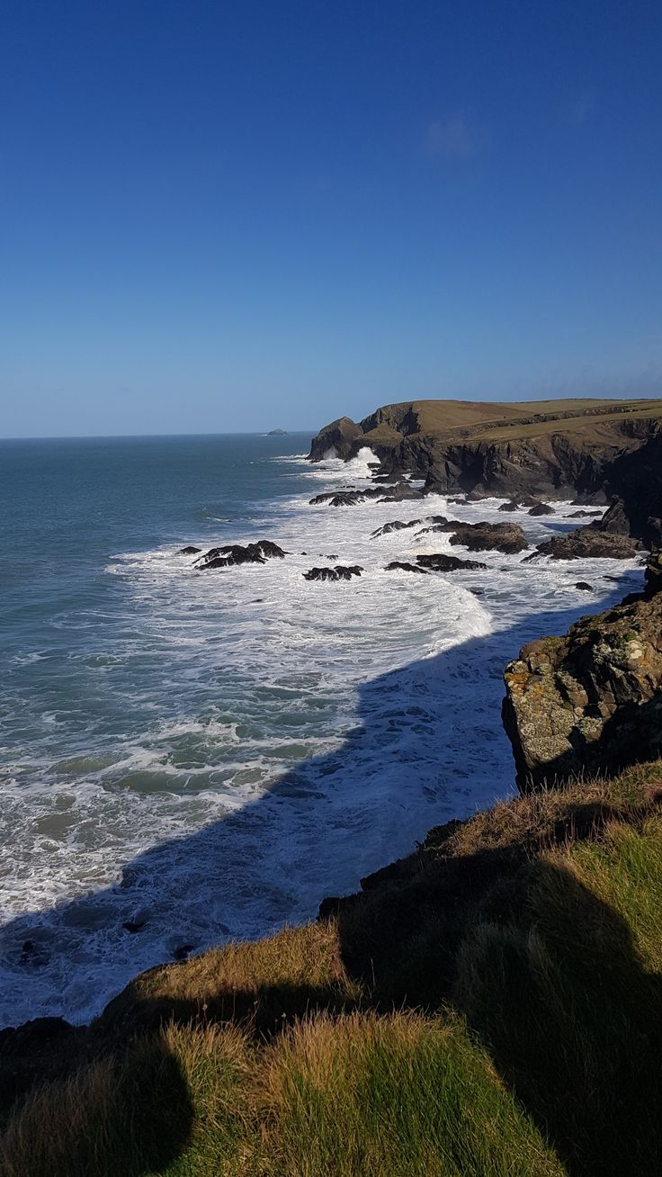 an ocean view with waves crashing on the shore and cliffs in the distance, under a blue sky