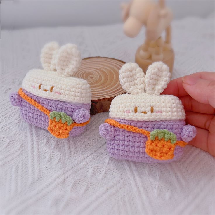 two small crocheted toy cars sitting on top of a white table next to a wooden slice