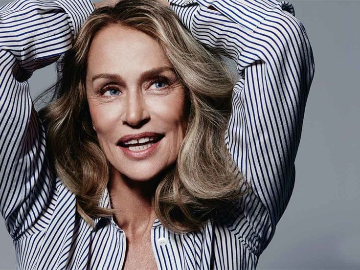 an older woman with blonde hair and blue striped shirt posing in front of a gray background