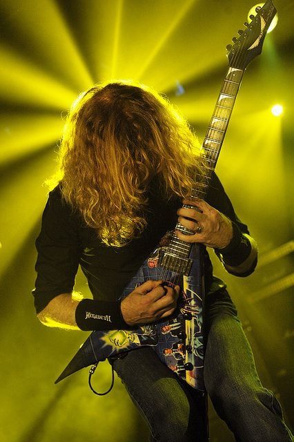 a man with long hair holding a guitar in front of yellow lights and spotlights