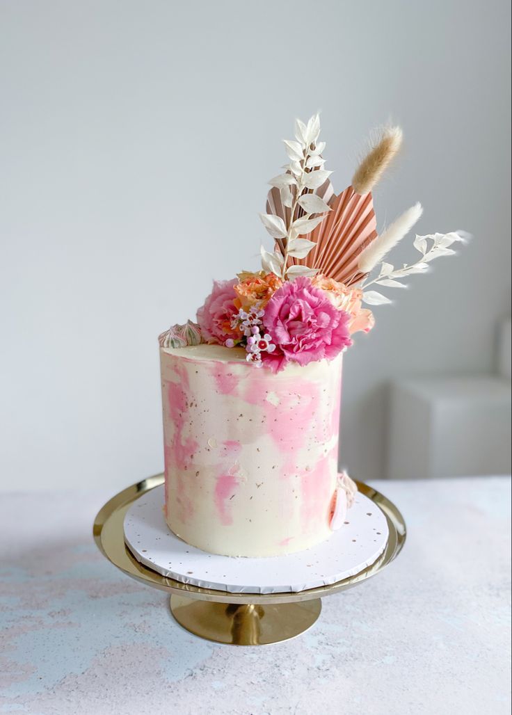 a pink and white cake with feathers on top is sitting on a gold platter