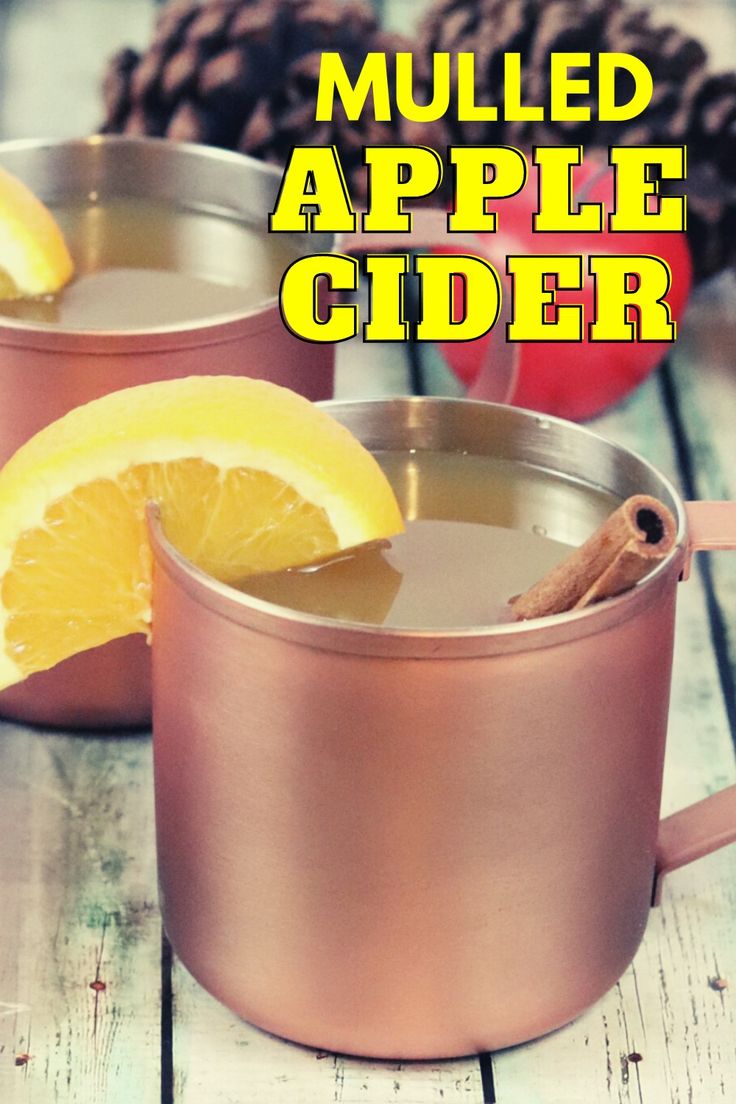 two mugs filled with apple cider sitting on top of a wooden table next to an orange slice