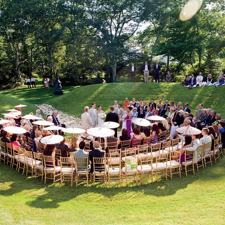 a large group of people sitting in chairs on top of a lush green field next to trees