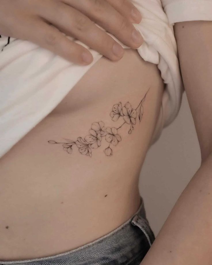 a close up of a person's stomach with flowers tattooed on the side and behind her