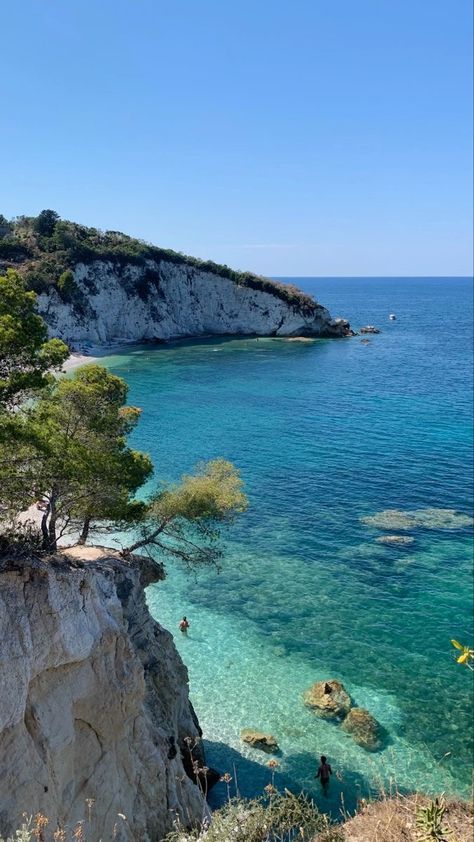 people are swimming in the clear blue water near an island with trees and cliffs on either side