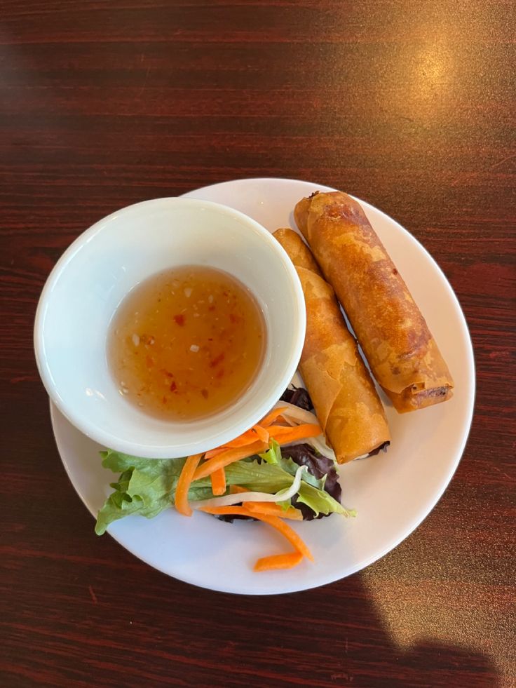 a white plate topped with food next to a bowl filled with soup and dipping sauce