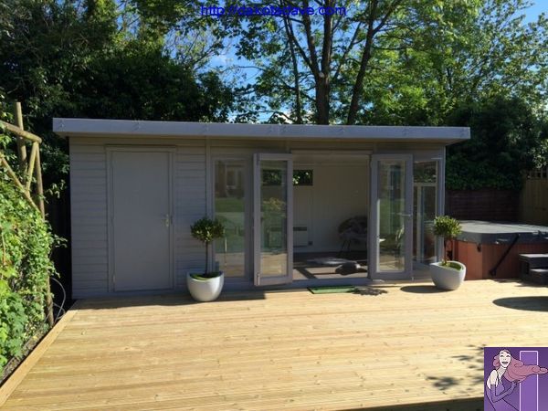 a wooden deck with a hot tub and table in the back ground area, surrounded by greenery