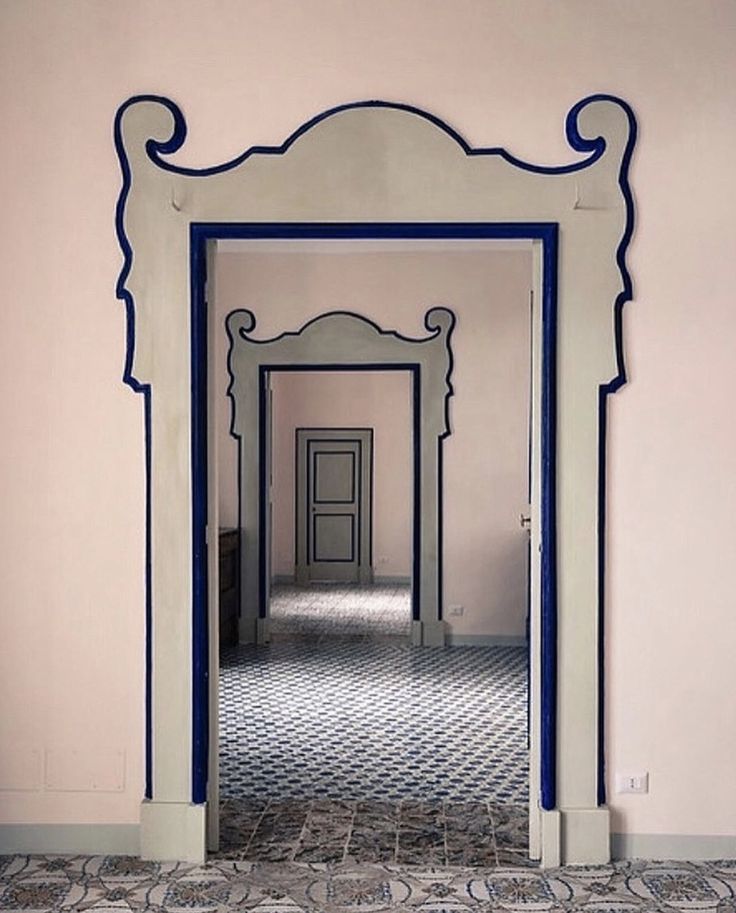 an ornate doorway with blue trim in a pink walled hallway, leading to another room