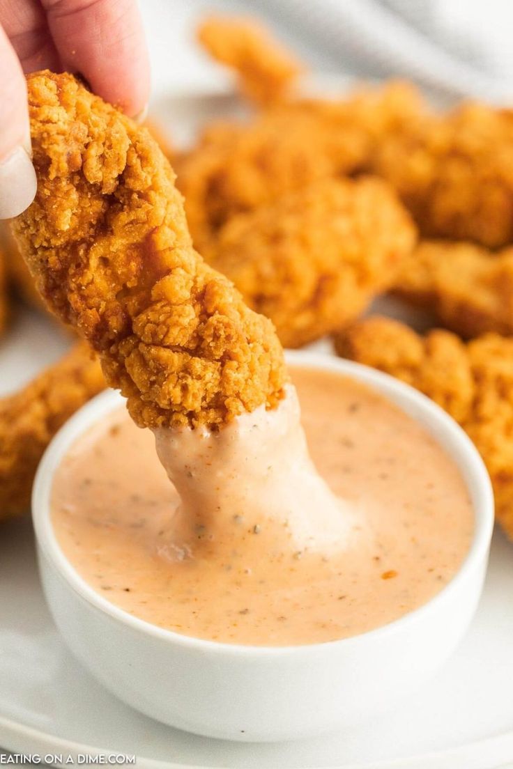 a person dipping something into a small white bowl filled with ranch sauce and fried chicken nuggies