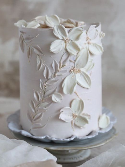 a white wedding cake decorated with flowers and leaves on a silver platter next to napkins